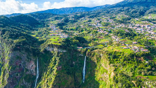 Valokuva Aerial view of a vibrant village nestled on Madeira's lush green cliffs, with dramatic waterfalls cascading into the Atlantic