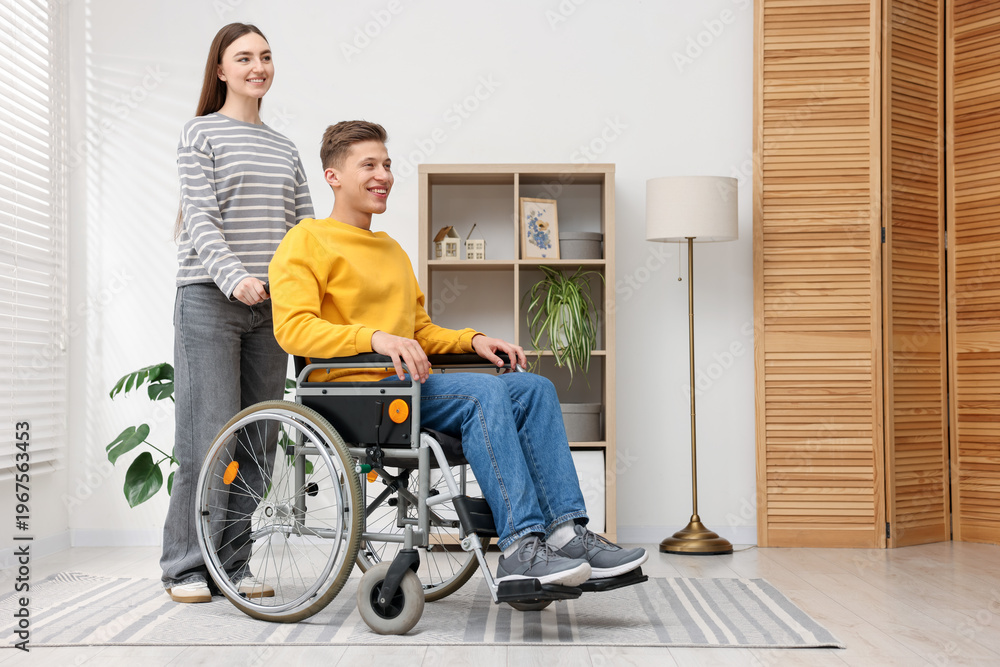 Fototapeta premium Man in wheelchair with woman at home. Space for text