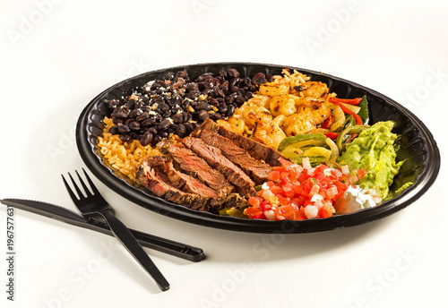 Steak and seafood fajita platter with black beans, rice, shrimp, salsa, guacamole, and sour cream in a black carry-out container on a white surface; copy space