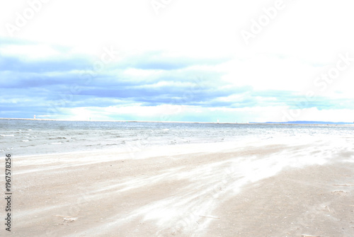 Bild auf Leinwand A wide, sandy beach is covered in blowing sand under a cloudy sky