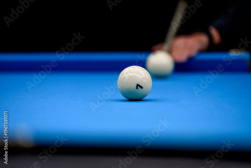 Close-up of billiard ball number 7 on blue pool table with cue stick