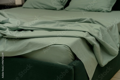 Soft green bedding on modern bed with rumpled sheets and pillows