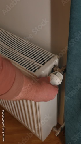 Hand adjusting radiator thermostat from low to high level, controlling indoor temperature and optimizing energy use at home.
