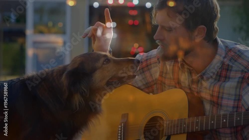 Man pausing guitar strumming after dog nudging, petting dog for bonding, warm bokeh on glass, music