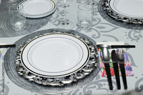 Elegant dining table set for eight with white tablecloth, silver charger plates, glassware and cutlery arranged for formal dinner at home