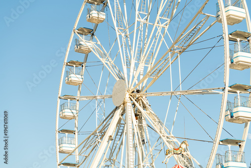 Large Ferris wheel adorned with colorful cabins rotates against a bright blue sky. Families and friends enjoy the thrill of riding it during a lively afternoon at a local carnival.