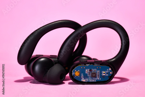 Open wireless earbud showing its internal circuitry on a pink background