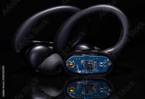 Open wireless earbud displaying its internal circuitry on a black background