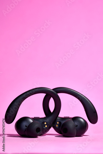 Wireless ear-hook headphones on a pink background in a minimalist composition