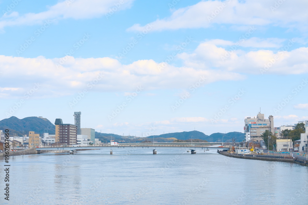 Fototapeta premium 穏やかな川面に架かる橋、水辺の街並みと遠景の山々