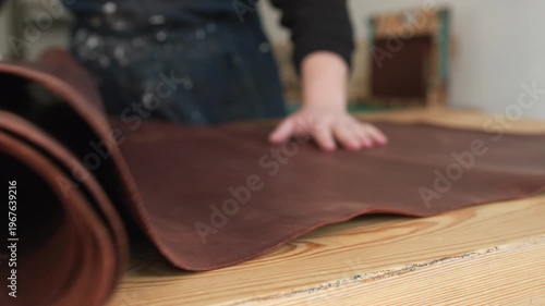 Leatherworker unrolling genuine brown leather on a wooden table