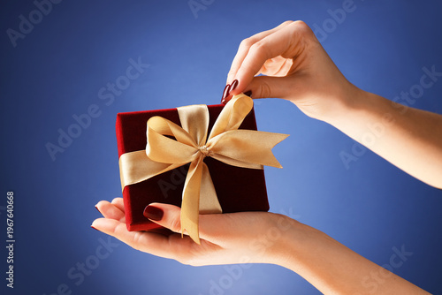 Woman holding beautiful gift box against blue background, closeup