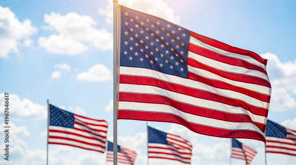 Obraz premium American Flags Waving in the Wind Against a Blue Sky with Sun Flare