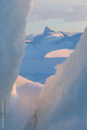 Winter arctic landscape. View of large ice hummocks and snowdrifts. The frozen sea. Cold frosty winter weather. The harsh climate of the polar region. Shallow depth of field. Blurred foreground.