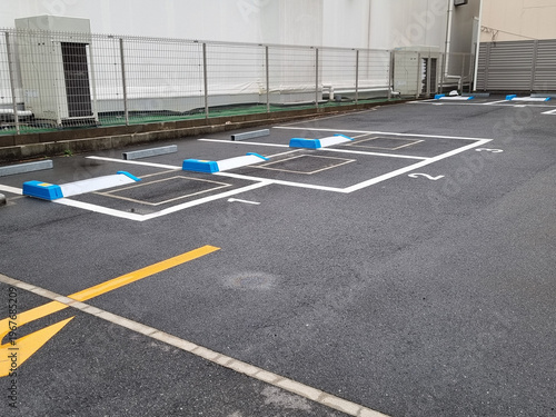 Empty automated coin parking lot in Japan with blue and white locking plate mechanisms. Numbered parking spaces on asphalt surface near a metal fence and industrial building. Professional shot.