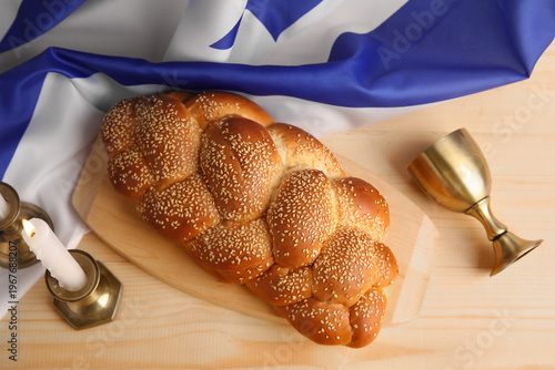 Фотография Traditional challah bread with flag of Israel, wine goblet and burning candles on table