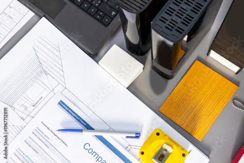 A design engineer's desk with construction drawings, a laptop, and materials placed on the desk.