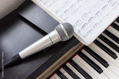 The close-up image shows a microphone placed on a piano with sheet music open above, suggesting a music practice, singing, or performance in a studio or home.
