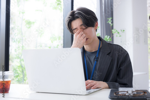 仕事の疲れで目を押さえる若手社員のストレスと体調不良のシーン　眼精疲労や目の疲れのビジネスイメージ