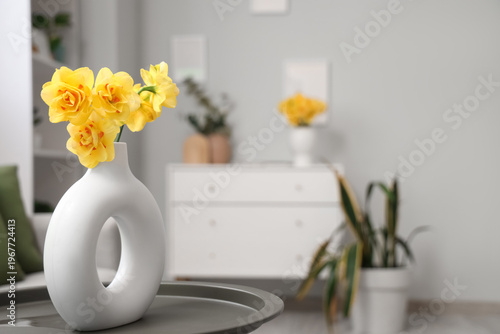 Vase with bouquet of beautiful narcissus flowers on coffee table in living room, closeup