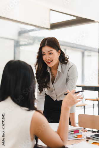 Smiling female manager discussing project paperwork with a colleague at a desk in a modern office Free Download Smiling female manager discussing project paperwork with a colleague at a desk in a modern office - GFXLoad