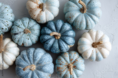 Various blue and white pumpkins are artistically arranged on a light surface. The pumpkins have unique textures and shades, creating an appealing autumn display.
