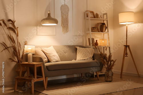 Cozy sofa, shelving unit and glowing lamps in interior of living room