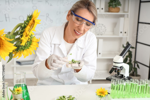 Happy female scientist with sunflower seeds, sprouts, flasks and test tubes o...