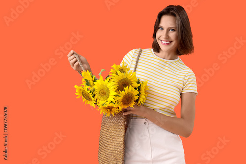 Beautiful young happy woman with wicker bag and bouquet of sunflowers on oran...