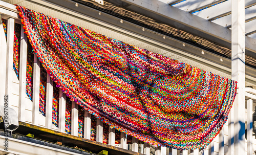 Colourful traditional braided rag rug with hit or miss pattern draped over white balcony railing airing in spring sunshine.