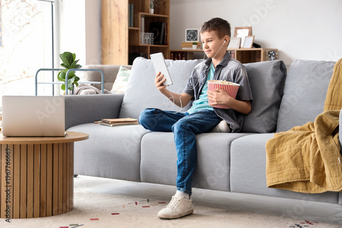 Teenage boy with tablet and popcorn watching film on sofa in living room