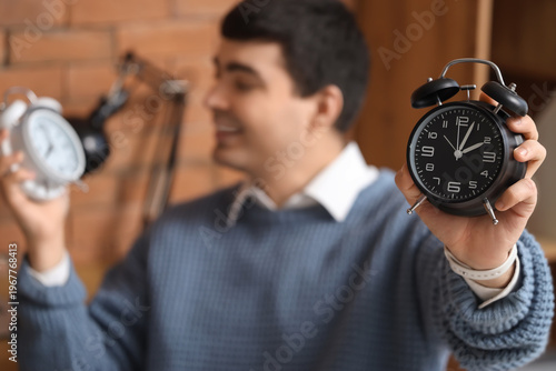 Young businessman with alarm clocks in office, closeup