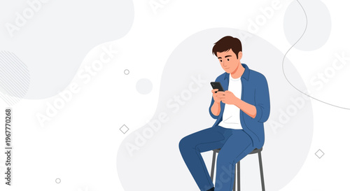 Young man in casual blue denim outfit using smartphone while sitting on stool, minimalist background