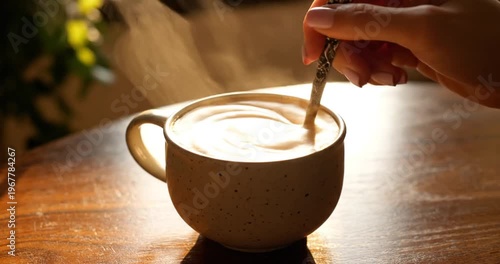 A cozy scene of a hand stirring a steaming cup of coffee on a wooden table with soft lighting
