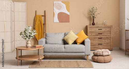 Sofa with dresser, coffee table and vase of white blooming branches near beige wall in living room
