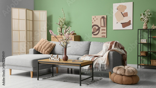 Sofa with coffee table, shelving unit and vases of blooming branches near green wall in living room