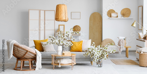 Interior of light living room with sofa, armchair and flowering branches in vases