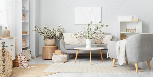 Interior of light living room with sofa, armchair and flowering branches
