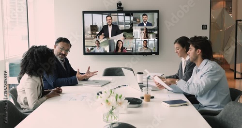 Diverse international business team discussing teamwork, work strategy, planning deal, partnership on online hybrid video conference, meeting at table and large screen, talking