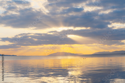 水面に映る夕焼けと光芒、静寂な湖畔の風景