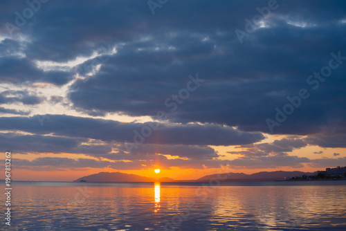 黄金色の夕日が水面に反射する夕暮れの湖畔と連なる山並みの風景