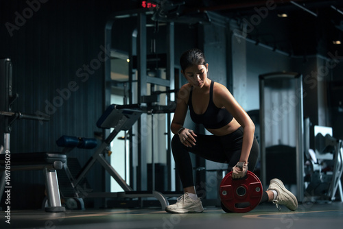 Sporty woman doing exercises with heavy weights plates in gym.