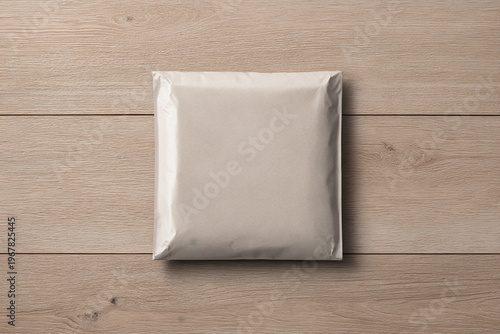 Top view of a blank square mailing envelope or padded poly mailer mockup resting on a light wood surface.
