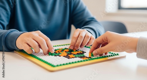 Hands rapidly placing small, colorful plastic tiles onto a grid to create a picture. Medium shot showing the rapid picking and placing motion in a bright, modern classroom.