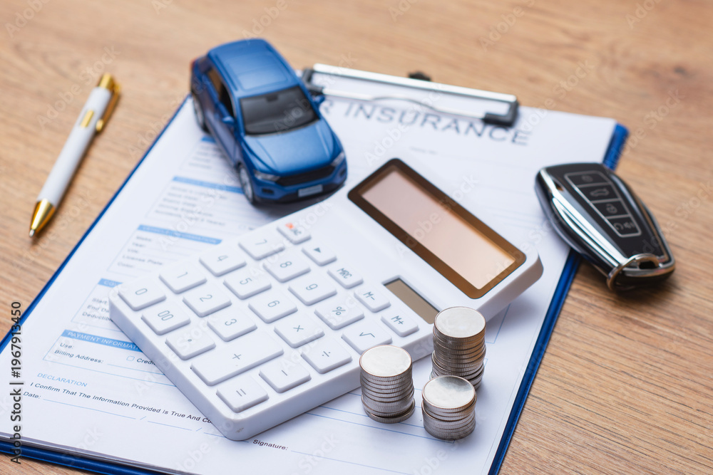 Obraz premium Car insurance document on clipboard with white calculator, stacked coins, blue toy car and modern car key on wooden desk. Concept auto insurance premium calculation and vehicle finance planning.
