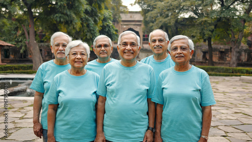 Group of seniors standing together in courtyard wearing matching shirts after volunteer activity. Community teamwork concept