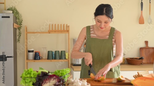 Woman cutting fresh papaya on a wooden board in a warm kitchen, preparing healthy food with natural ingredients.