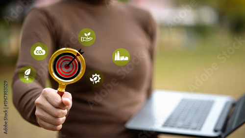 Businessman holding magnifying glass focusing on bullseye target with ESG and carbon neutral icons.