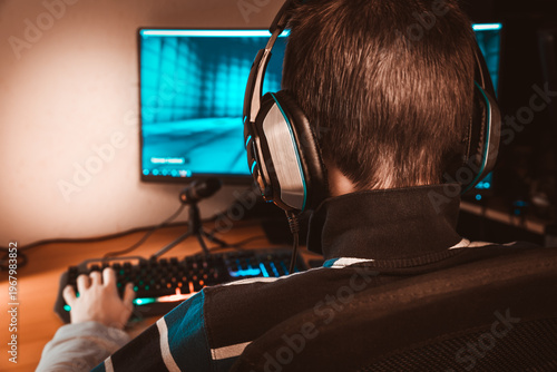 Teenager in headphones playing video game on his computer