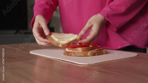 A housewife covers the sandwich with a top piece of bread and presses it down to put it on the grill.